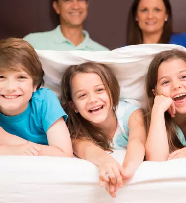 Happy family of hotel guests under clean sheets